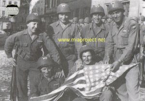 Kitzingen, Germany, May 1945. 1st Lt Samuel Lombardo and platoon members displaying the flag for a US Army photograph. Back Row: L to R: Pfc. Gordon Wetherby, Charlestown, NH; T/Sgt Isadore Rosen, Pittsburgh, PA; Pfc. George E. Bellaire, Dayton, OH; 1st Lt. Samuel Lombardo, Altoona, PA Front Row: Left to Right: Corp. Cury Beauvais, Chicopee Falls, MA; S/Sgt William Junod, Wyandotte, MI